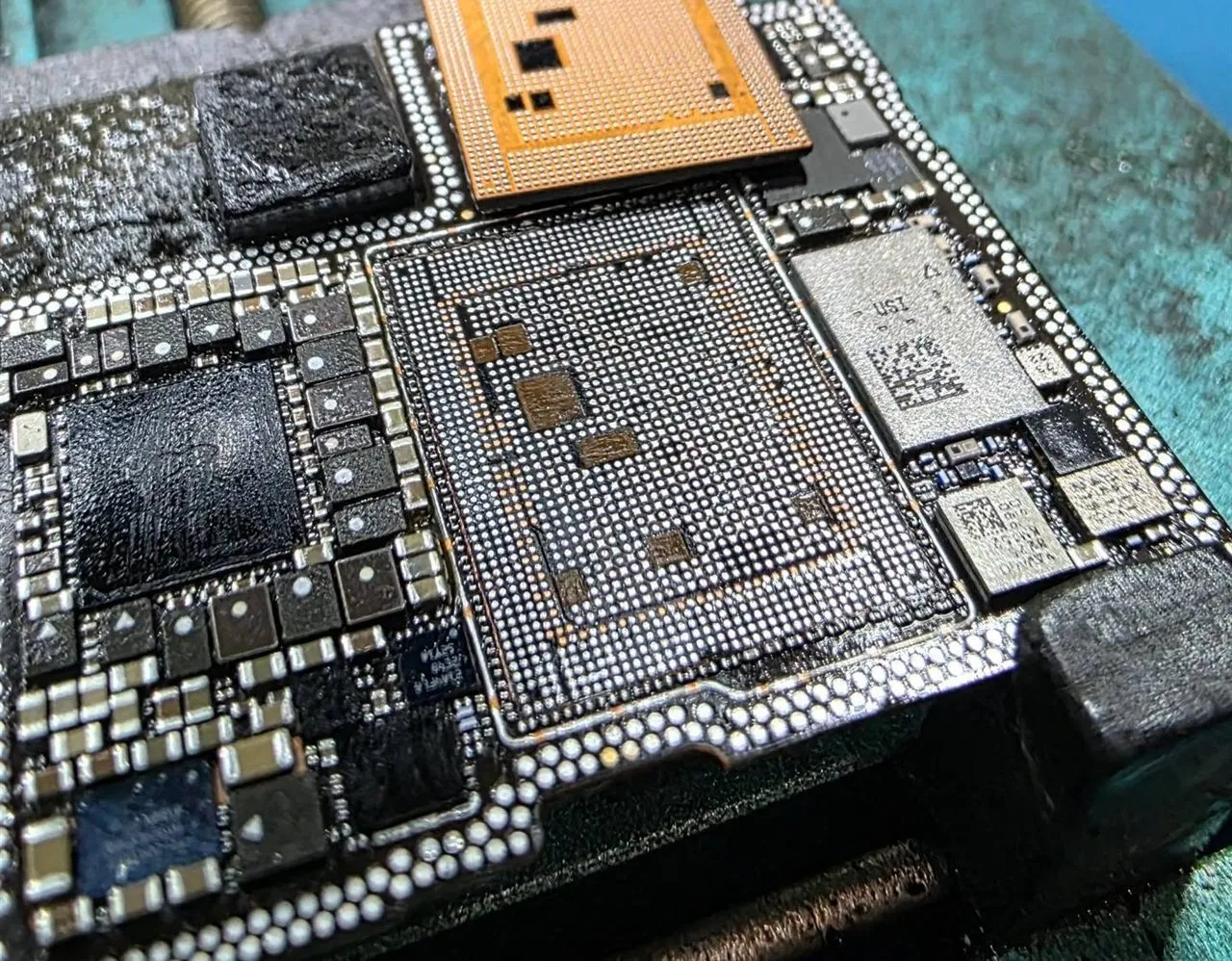 Tarjeta lógica de iPhone bajo el microscopio, con un chip retirado para volver a soldarlo