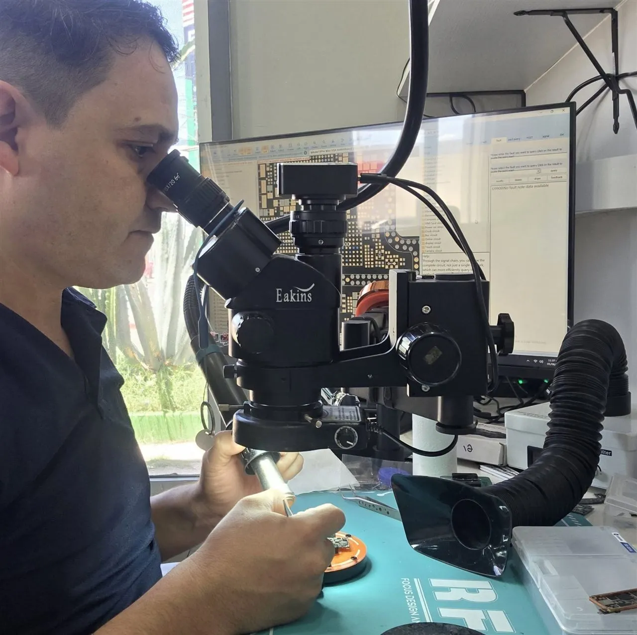 Técnico de JM soldando una placa de iPhone bajo el microscopio, con el diagrama del circuito en pantalla